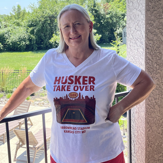 Person wearing a white t-shirt with 'Husker Take Over' design on a balcony.